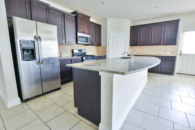 kitchen with an island with sink, stainless steel appliances, backsplash, sink, and light stone countertops