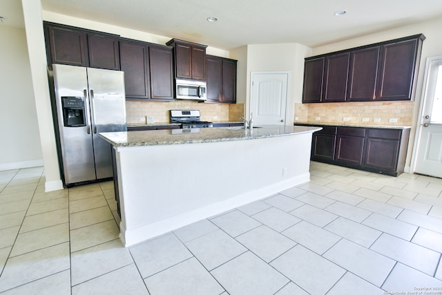 kitchen with appliances with stainless steel finishes, tasteful backsplash, light stone counters, and a center island with sink