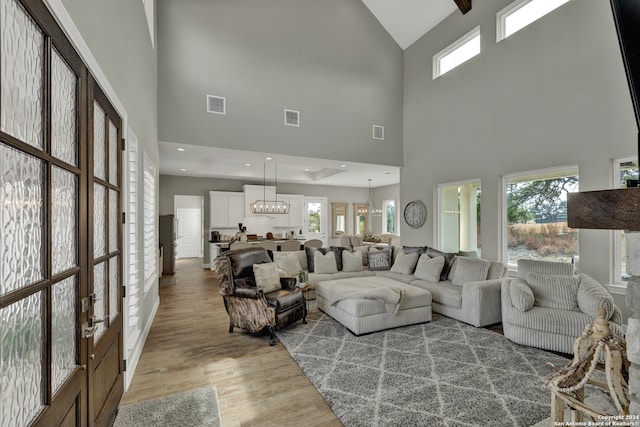 living room with a healthy amount of sunlight, a notable chandelier, hardwood / wood-style flooring, and a towering ceiling