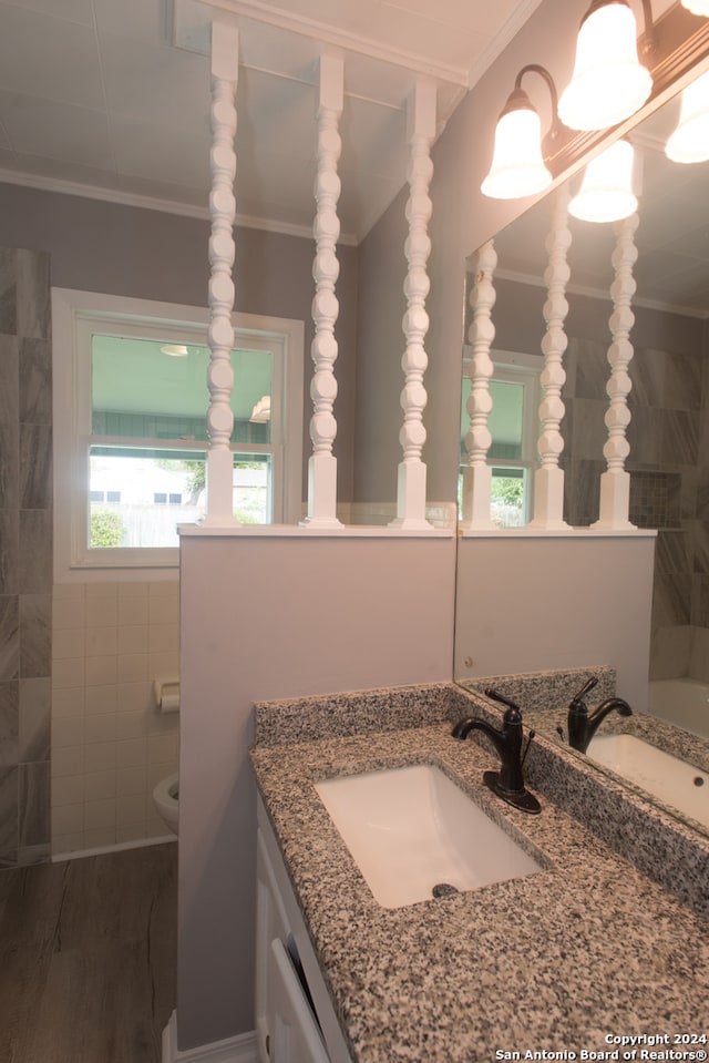 bathroom featuring wood-type flooring, toilet, tile walls, vanity, and ornamental molding