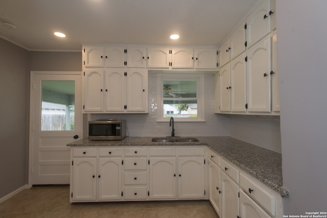 kitchen with decorative backsplash, white cabinetry, light tile patterned flooring, stone counters, and sink