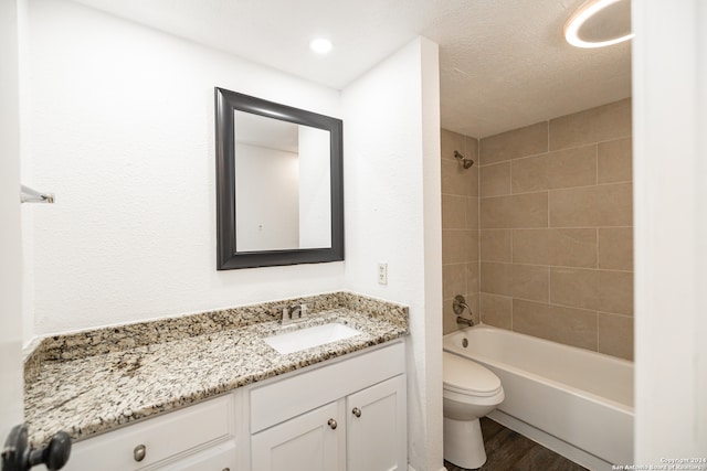 full bathroom with tiled shower / bath, hardwood / wood-style floors, a textured ceiling, toilet, and vanity