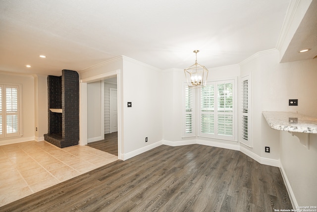 unfurnished dining area featuring hardwood / wood-style floors, a brick fireplace, crown molding, and a chandelier