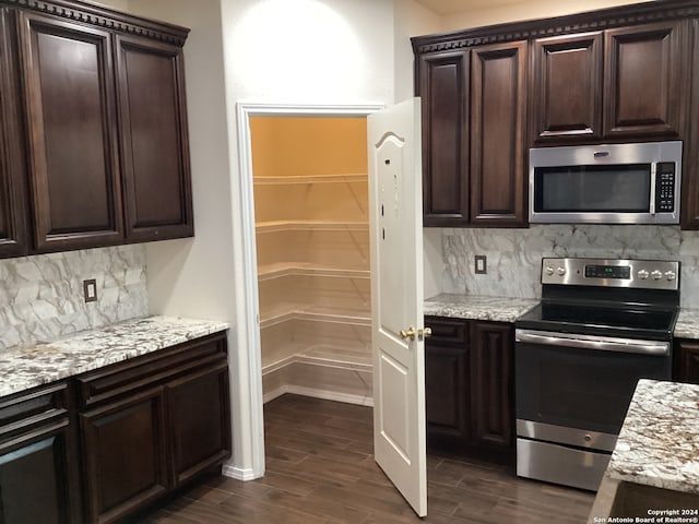 kitchen featuring dark brown cabinetry, appliances with stainless steel finishes, backsplash, and dark wood-type flooring