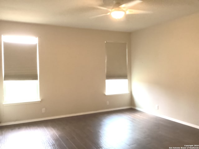 spare room with a ceiling fan, dark wood-style flooring, plenty of natural light, and baseboards