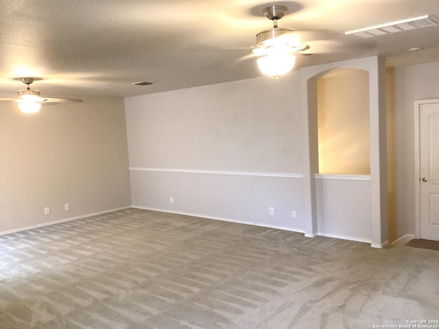 carpeted spare room with ceiling fan, visible vents, and arched walkways