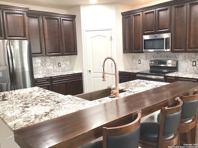 kitchen featuring dark brown cabinetry, appliances with stainless steel finishes, backsplash, and a sink