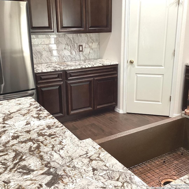 bar featuring dark wood-type flooring, freestanding refrigerator, and backsplash