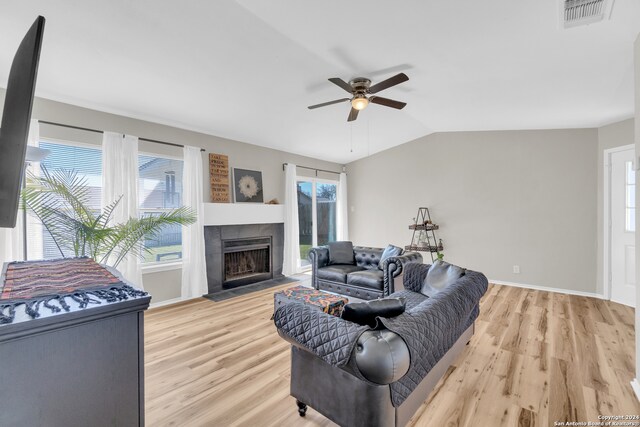 living room with light wood-type flooring, vaulted ceiling, plenty of natural light, and a tile fireplace