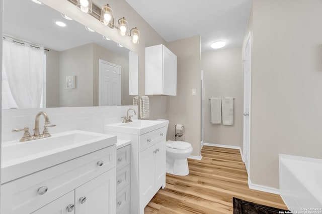 8722 Ridge Moon Dr, San Antonio, TX 78239 - bathroom featuring toilet, wood finished floors, backsplash, two vanities, and a garden tub