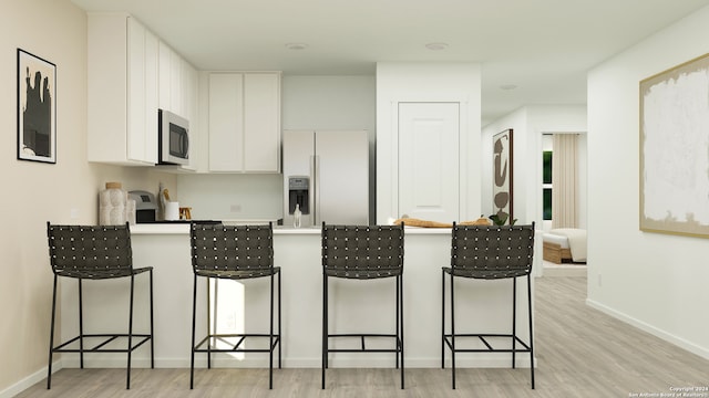 kitchen featuring white cabinetry, light hardwood / wood-style flooring, white refrigerator with ice dispenser, and a breakfast bar area