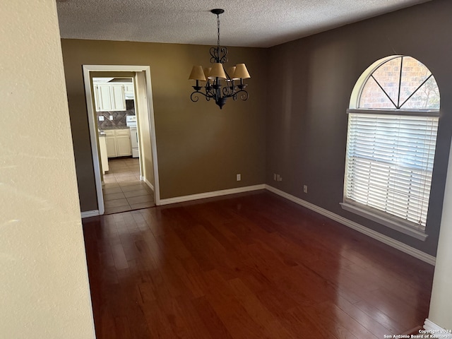 spare room with dark hardwood / wood-style flooring, a textured ceiling, and an inviting chandelier