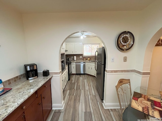 kitchen featuring appliances with stainless steel finishes, ceiling fan, white cabinets, light stone counters, and light hardwood / wood-style flooring