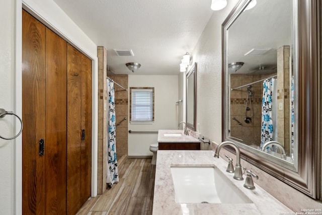 bathroom featuring vanity, toilet, a tile shower, visible vents, and wood finished floors