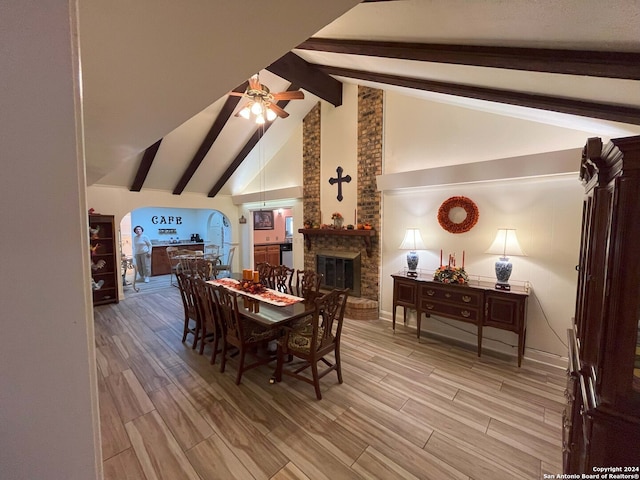 dining space with light wood-type flooring, a fireplace, ceiling fan, beam ceiling, and high vaulted ceiling