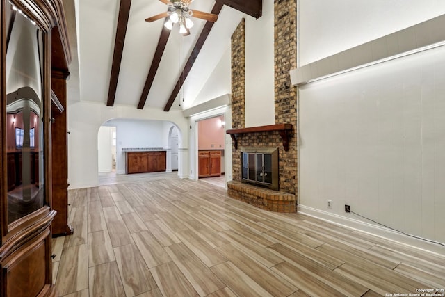 unfurnished living room with arched walkways, a ceiling fan, beamed ceiling, and a fireplace