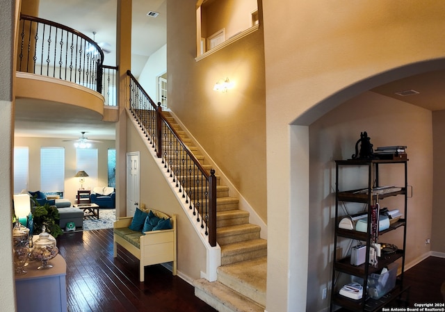 stairs featuring a towering ceiling, hardwood / wood-style flooring, and ceiling fan