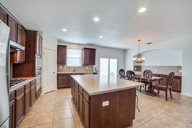 kitchen with a kitchen island, stainless steel appliances, pendant lighting, light tile patterned floors, and a chandelier