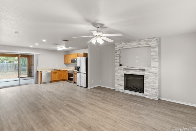 unfurnished living room featuring light hardwood / wood-style floors, sink, a fireplace, and ceiling fan