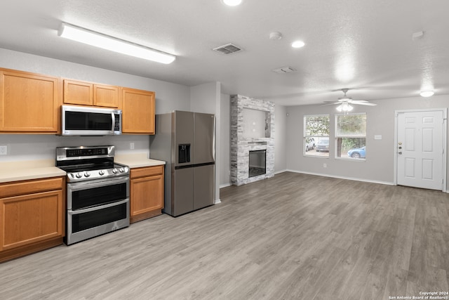 kitchen with appliances with stainless steel finishes, a fireplace, light wood-type flooring, and ceiling fan