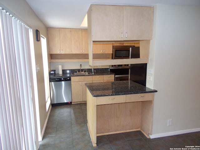 kitchen featuring dark stone countertops, stainless steel appliances, sink, and light brown cabinets