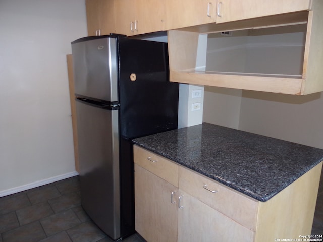 kitchen featuring dark stone countertops, light brown cabinets, and stainless steel fridge