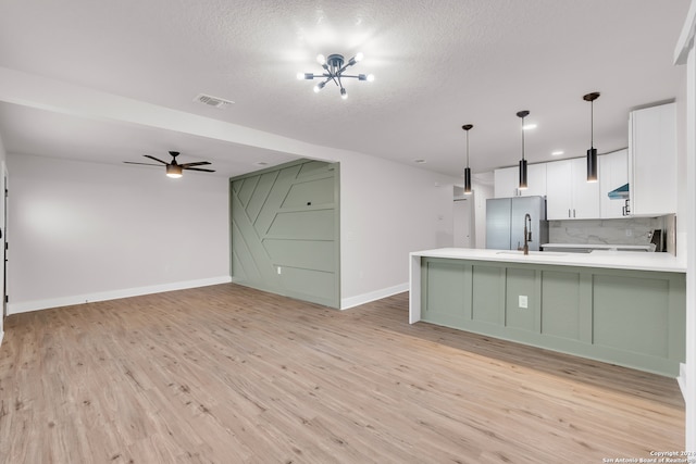 kitchen with kitchen peninsula, pendant lighting, white cabinets, light hardwood / wood-style floors, and stainless steel refrigerator