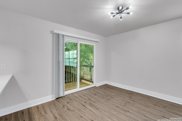 unfurnished room featuring an inviting chandelier, a textured ceiling, and light hardwood / wood-style floors