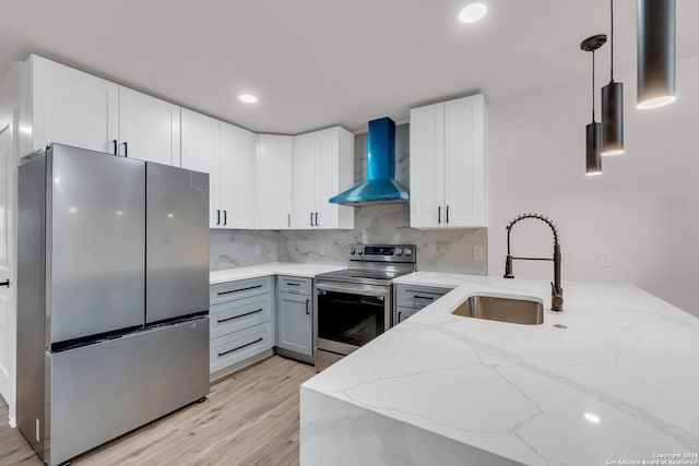 kitchen with light hardwood / wood-style floors, wall chimney exhaust hood, stainless steel appliances, and hanging light fixtures