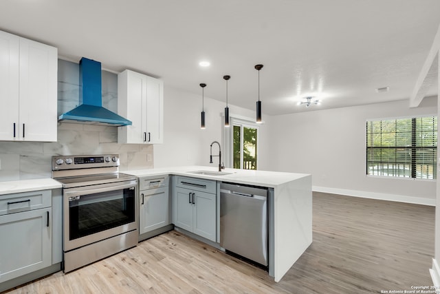 kitchen featuring wall chimney range hood, appliances with stainless steel finishes, light stone countertops, light hardwood / wood-style flooring, and sink