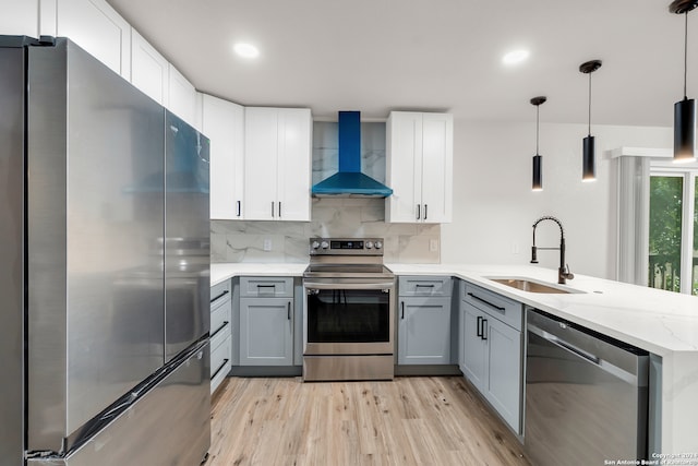 kitchen with sink, kitchen peninsula, stainless steel appliances, wall chimney exhaust hood, and pendant lighting