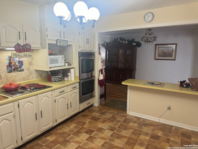 kitchen featuring stainless steel appliances, pendant lighting, white cabinets, decorative backsplash, and an inviting chandelier