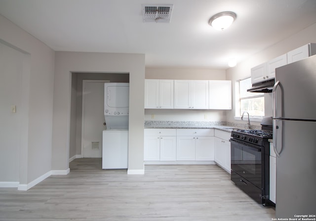 kitchen featuring gas stove, white cabinetry, light wood-type flooring, stacked washer and dryer, and white fridge