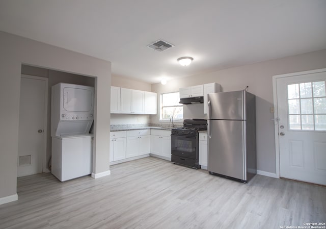 kitchen featuring white cabinets, stainless steel fridge, black gas range, light hardwood / wood-style flooring, and stacked washer / drying machine