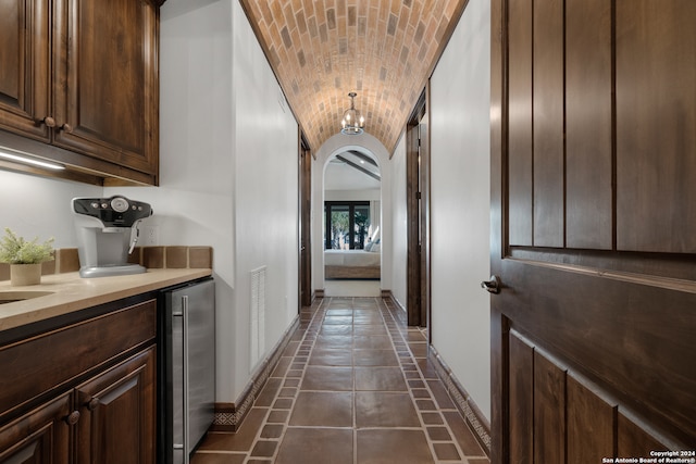 hall featuring dark tile patterned flooring, wine cooler, brick ceiling, and lofted ceiling