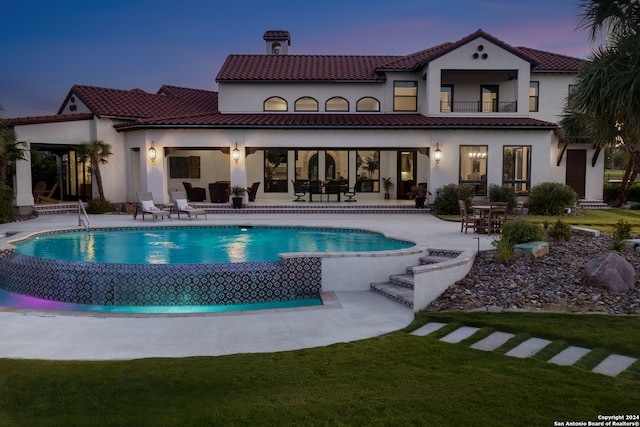 back house at dusk featuring a patio area and a lawn