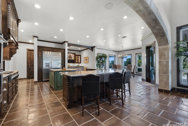 kitchen with light stone countertops, a spacious island, built in fridge, a notable chandelier, and a breakfast bar area