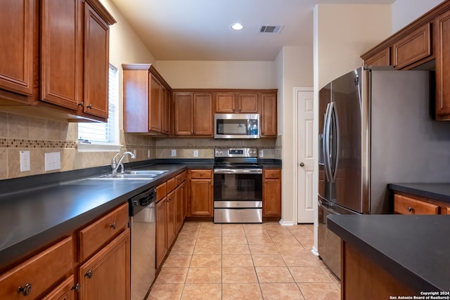 10707 Axis Xing, San Antonio, TX 78245 - kitchen featuring stainless steel appliances, a sink, dark countertops, light tile patterned floors, and brown cabinetry