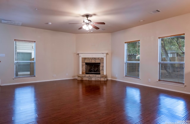 unfurnished living room featuring a stone fireplace, ceiling fan, a healthy amount of sunlight, and dark hardwood / wood-style flooring