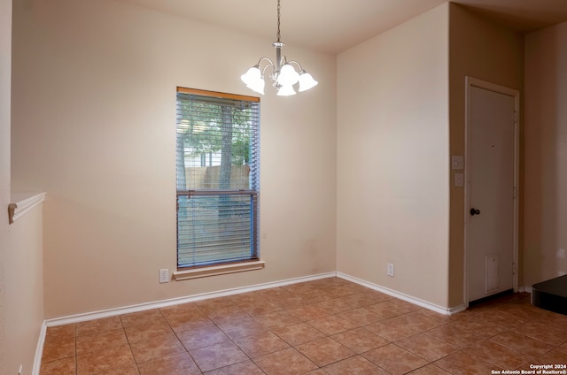 tiled spare room with a chandelier