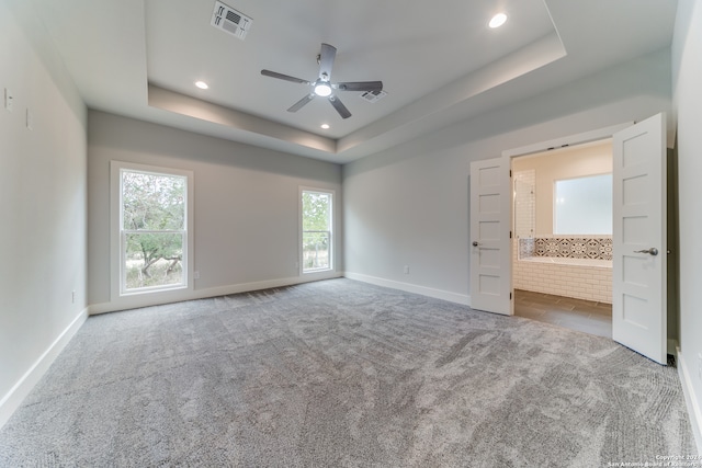 unfurnished bedroom with a raised ceiling, ceiling fan, carpet floors, and multiple windows