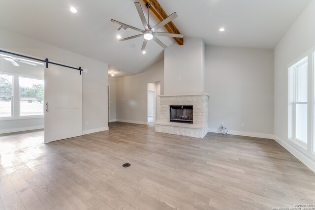 unfurnished living room with beamed ceiling, a fireplace, light wood-type flooring, ceiling fan, and a barn door