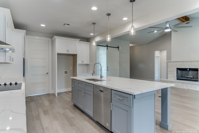 kitchen featuring tasteful backsplash, a barn door, dishwasher, a kitchen island with sink, and light stone counters