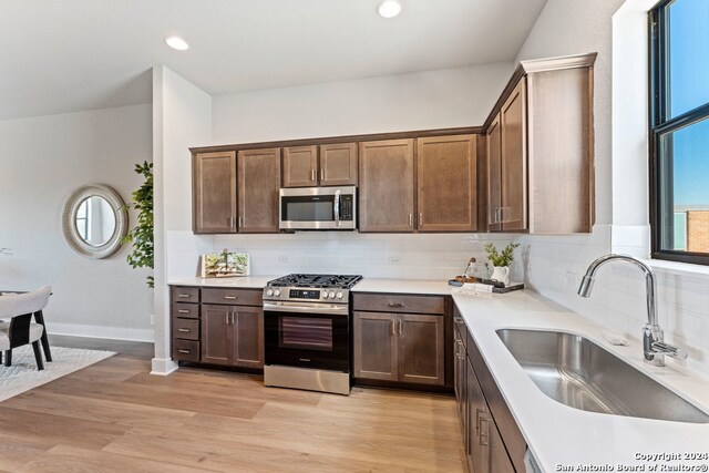 kitchen with tasteful backsplash, appliances with stainless steel finishes, sink, and light wood-type flooring