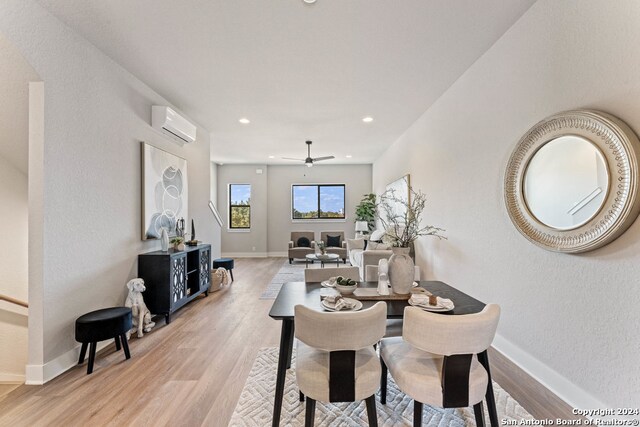 dining space with a wall mounted air conditioner, light wood-type flooring, and ceiling fan