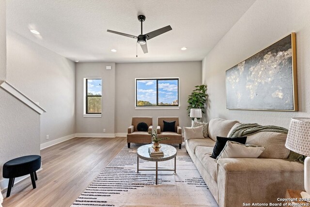 living room with light hardwood / wood-style flooring, a textured ceiling, and ceiling fan