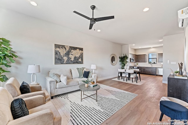 living room featuring a wall mounted AC, light hardwood / wood-style flooring, and ceiling fan