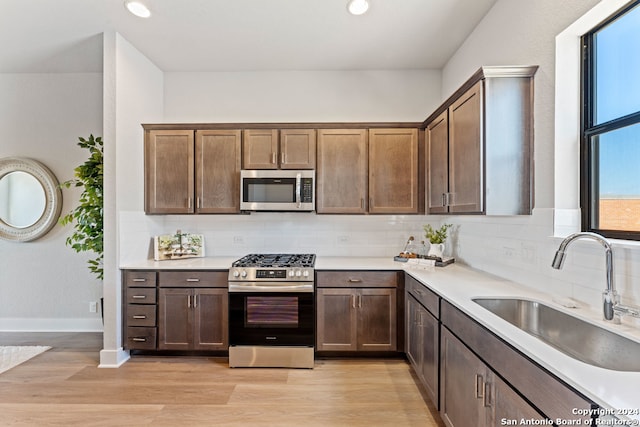 kitchen with tasteful backsplash, sink, dark brown cabinets, stainless steel appliances, and light hardwood / wood-style flooring