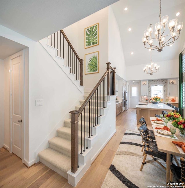 stairs with high vaulted ceiling, sink, an inviting chandelier, and hardwood / wood-style floors