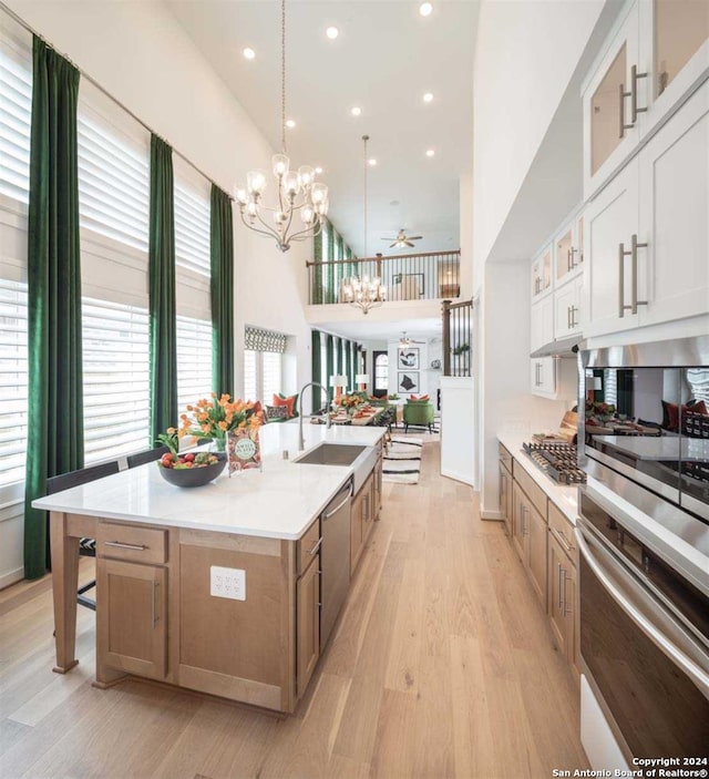 kitchen with a large island with sink, sink, ceiling fan, white cabinets, and light wood-type flooring